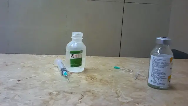 Hay dos botellas sobre la encimera, junto a lo que parece ser una aguja y una jeringuilla tiradas.