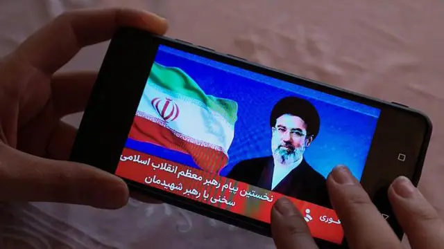 Una mujer sostiene un teléfono mientras que en su pantalla se ve una imagen del líder supremo de Irán.