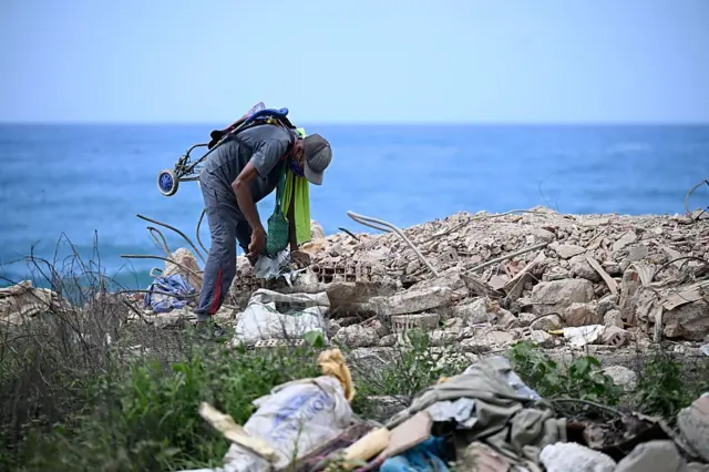 Un hombre se agacha y parece buscar entre los escombros que dejó el sismo. Detrás, el mar. 